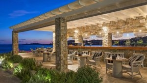 restaurant mit vielen rohen steinen und geschliffenen steinen als boden fliesen die tische und stühle sind aus wie ein korb geflochten und das überdachte restaurant bietet einen atemberaubenden ausblick auf das dunkel blaue meer am abend im luxuriösen hoc